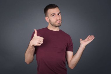 Genç, mutlu, neşeli bir adam baş parmağını gösterip diğer elini de evin içinde dururken işaret ediyor. İyi iş çıkardın. Günlük giysiler giyiyor..