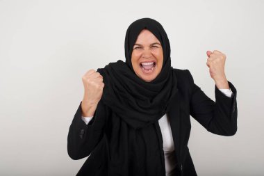 Güzel, orta yaşlı, tesettürlü Müslüman kadının portresi kameraya heyecanla bakıyor, ellerini başının üstüne kaldırıyor, beklenmedik bir şey fark ediyor, duvarın üzerinde izole edilmiş.. 