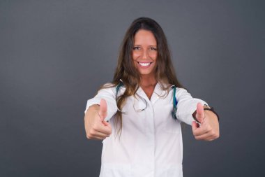 İyi iş! Mutlu gülümseyen genç bir doktorun portresi. Başarılı genç bir kadın. Kapalı alanda iki parmak hareketi yapıyor. Olumlu insani duygu yüz ifadesi vücut dili. Komik kız.