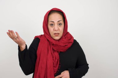 What the hell are you talking about, nonsense. Studio shot of frustrated female gesturing with raised palm, frowning, being displeased and confused with dumb question over gray wall. Middle-aged Arab woman wearing head scarf posing in studio