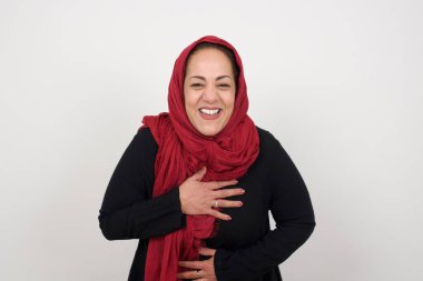 Neşeli olgun Müslüman kadın ellerini çapraz yapar, güzel şakalara güler, günlük kıyafetler giyer ve gözlük takar, kapalı yerde durur.. 