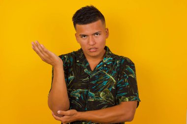 What the hell are you talking about, nonsense. Studio shot of frustrated hispanic male with blond hair gesturing with raised palm, frowning, being displeased and confused with dumb question over  wall.