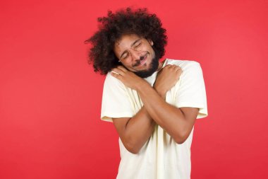 Kızıl duvarda kendine sarılan afro saçlı genç adam.   