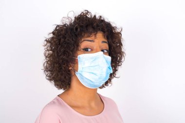 Yüz maskesi takan ve beyaz stüdyo arka planında izole edilmiş günlük kıyafetler giyen bir kadın.