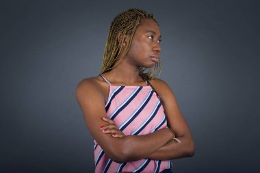 İçeride kollarını kavuşturmuş, üzgün, Afro-Amerikan bir kadının görüntüsü. Gri stüdyoda duruyor..