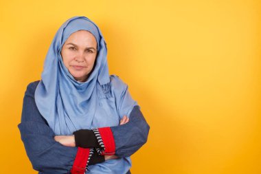 Güzel, kendine güveni yüksek orta yaşlı, tesettürlü Müslüman bir kadının belinde geniş bir gülümseme, kollarını kavuşturur.