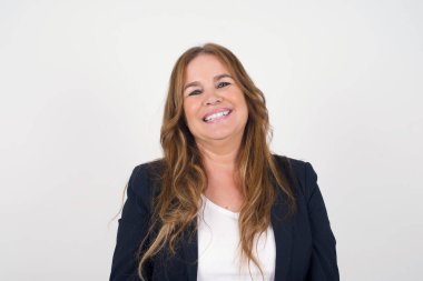 Güzel, gülümseyen, orta yaşlı, geniş gülüşlü, beyaz dişli, sıradan tişörtlü, gri stüdyo duvarının üzerinde duran, izin gününün keyfini çıkaran bir kadın. Kadın içeride duruyor..