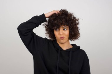 Tüh, ne yaptım ben? Güzel bir kadın korkmuş ve pişmanlık dolu bir ifadeyle el ele tutuşuyor. Gri arka planda dikilen günlük giysiler giyiyor..