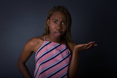 Studio shot of frustrated young african american woman over gray background gesturing with raised palm, frowning, being displeased and confused with dumb question over gray wall. 