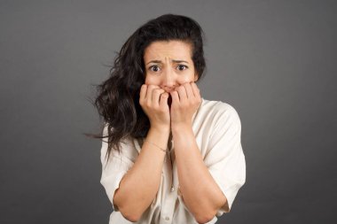 Gayri resmi giyinmiş güzel esmer kadın korkuyor. Gri arkaplanda duruyor.  