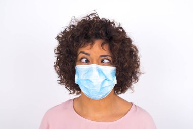 Yüz maskesi takan ve beyaz stüdyo arka planında izole edilmiş günlük kıyafetler giyen bir kadın.