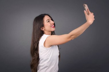 Güzel bir kadın selfie çekiyor. Gri arkaplanda duruyor. 