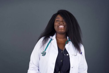 Güzel görünümlü Afro-Amerikan kadın doktorun yatay portresi yüzünü saçlarla örterek kameraya mutlu bir şekilde bakıyor..