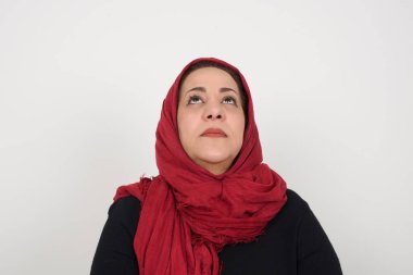 Gizemli bir gülümsemeyle yukarı bakan gizemli bir kadının portresi. Stüdyoda poz veren başörtüsü takan orta yaşlı bir Arap kadın.