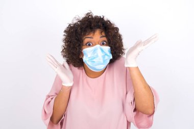  Yüz maskesi takan kafası karışık bir kadın ve beyaz stüdyo arka planında izole edilmiş günlük kıyafetler.