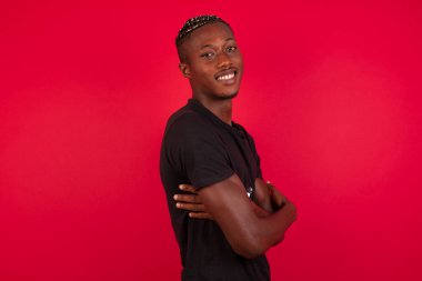 Kırmızı arka planda siyah tişört giyen, kolları bağlı, neşeli Afro-Amerikan bir adam resmi. Kameraya bakıp gülümsüyor. Kendine güvenen başarılı bir adam..