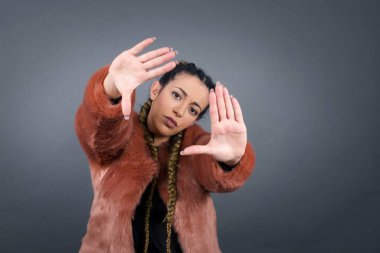 El hareketli parmak çerçevesi. Gülümseyen genç bir kadının portresi. Gri arka planda dururken kameraya ve işaret parmağına bakıyor.