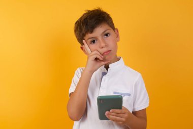 Akıllı telefonu sarı duvara dayayan sevimli çocuk.  