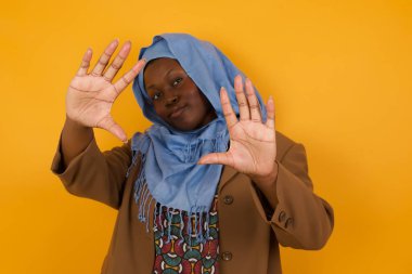 El hareketli parmak çerçevesi. Gülümseyen, Afro-Amerikan müslüman bir kadının portresi. Kameraya bakıyor ve el hareketi yapıyor.