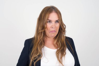 Güzel orta yaşlı bir kadın, burnu havada, dudaklarını kıvıran, kaşlarını kaldıran şüpheli ve şüpheci bir ifadeyle şüpheli ve şüpheci bir ifadeyle bakıyor. Gri arka planda kapalı duruyor..