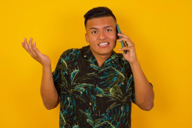 Sarı arka planda telefonla konuşan Latin asıllı genç bir adam. Yüzü kızarmış, utanmış ve şaşırmış bir halde. Kızgın ve sinirli. Hata için korku ve üzüntü.