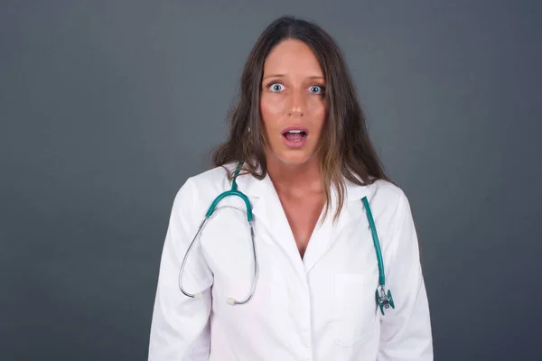 Aantrekkelijke Jonge Doktersvrouw Geïsoleerd Grijze Achtergrond Die Verbijsterd Geschokt Keek — Stockfoto