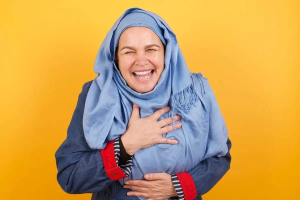ヒジャーブの楽しい中年のイスラム教徒の女性は 手を交差させ 良い冗談を笑い カジュアルな服や丸い光景を着て 屋内で立っています — ストック写真