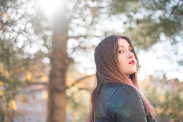 Parkta poz veren deri ceketli beyaz bir kadın.  