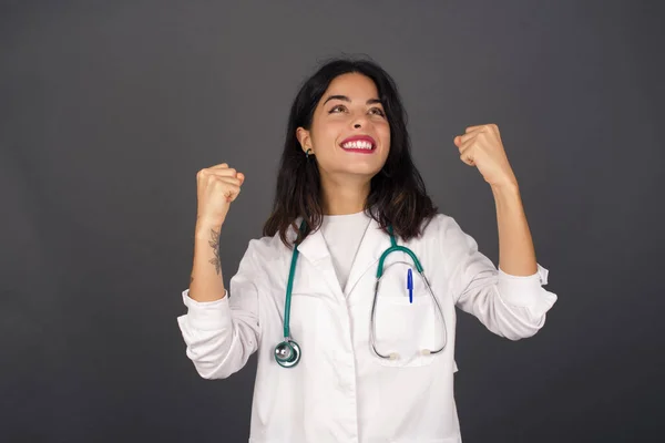 Excited young doctor woman winner raising his fists with great happiness having good mood after winning game. Young champion having success being glad to achieve her goals. Victory and triumph concept.