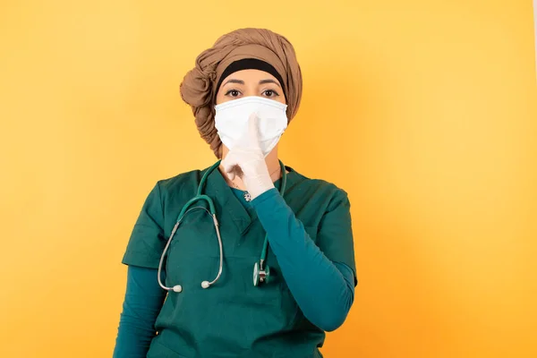 Don't tell my secret or not speak too loud, please! Emotional surprised young doctor woman wearing medical uniform makes hush gesture, asks be quiet.