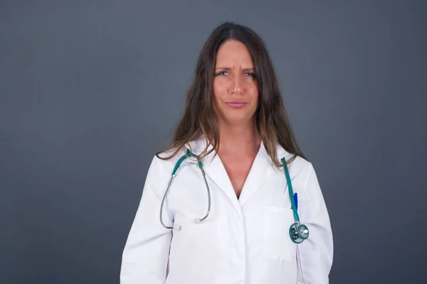 一个身穿医疗制服的愤怒的年轻医生的画像 皱着眉头对某件事感到不满 在灰蒙蒙的天空中被隔离的漂亮的女性 — 图库照片