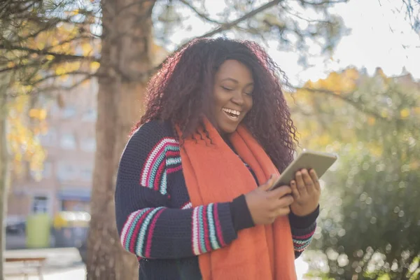 Güz parkında tablet kullanan uzun saçlı güzel Afro-Amerikan kadın renkli kazak giyiyor.  