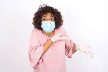 Yüz maskesi takan kafası karışık bir kadın ve beyaz stüdyo arka planında izole edilmiş günlük kıyafetler.