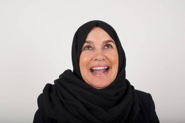 İnsanlar ve ani tepki kavramı. Siyah tesettürlü, şaşırmış Müslüman kadın omuz silkiyor, yana bakıyor, arkadaşlarıyla yeni planları için mutlu ve heyecanlı. Gri duvarda izole edilmiş..