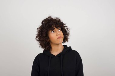 Sorunlu şaşkın kadın yüzünü ısırır, dudaklarını ısırır, kaşlarını kaldırır, yukarı bakar, sorunları olur, şık giyinir, gri arka planda izole olur, pişman olur..