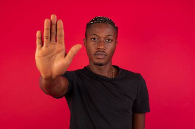 Genç, yakışıklı, Afro-Amerikan bir adam avuç içiyle jesti durduruyor. Arka planda izole edilmiş yüz üzerinde negatif ve ciddi jest içeren uyarı ifadesi.