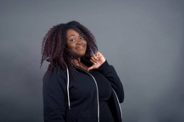 Neşeli, güzel, Afro-Amerikan kadınlarına yakın çekim neşeli, memnun ve kendinden emin görünüyor, başparmağıyla işaret ediyor, stüdyo arka planında izole edilmiş..