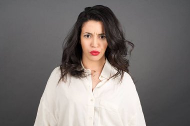 Gündelik giyinmiş güzel esmer kadın, gri arka plana karşı kızgın..  