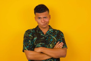 Sarı arka planda, kollarını kavuşturan öfkeli İspanyol adamın resmi. Hayal kırıklığına uğramış bir ifadeyle kameraya bakmak.