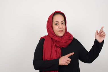 Olumlu ifadeli güzel esmer kadın, sıradan giyinmiş, promosyon metnin veya reklamın için boş fotokopi alanında ön parmağıyla işaret ediyor. Stüdyoda poz veren başörtüsü takan orta yaşlı bir Arap kadın.