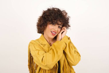 Tatlı yüzlü, hayalperest genç bir kadın, gözlerini kapatıyor, ellerini yüzüne çarpıyor, hoş bir şey düşünüyor, gri arka planda poz veriyor..