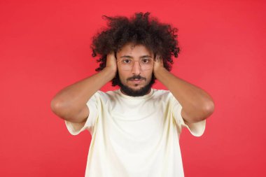 Kızıl duvara karşı kulaklarını kapatan afro saçlı genç adam.   