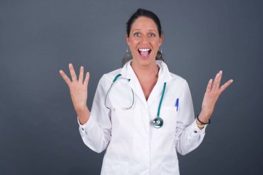 İnsanlar, başarı, galibiyet, zafer, heyecan, hedefler, kararlılık ve başarı konsepti. Neşeli, heyecanlı, şanslı doktor kadın. Gri arka planda izole edilmiş. Tezahürat yapıyor, başarıyı kutluyor.