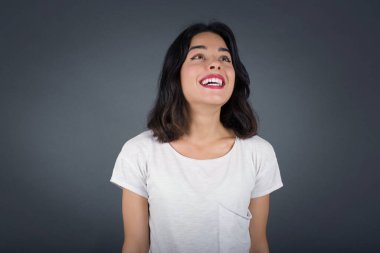 İnsanlar ve ani tepki kavramı. Şaşırmış Kafkasyalı güzel kız öğrenci, omuz silkiyor, yana bakıyor, arkadaşlarıyla yeni planları için mutlu ve heyecanlı. Gri duvarda izole edilmiş..