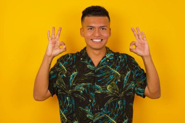 Çekici İspanyol erkeğin iki eliyle işaret dili göstermesine sevindim. Onaylıyor, neşeli bir ifadesi var, iyimser. Duvara yaslanarak.