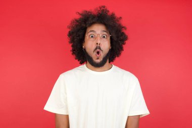Afro saçlı genç adamın kırmızı duvara karşı kafası karışık. 