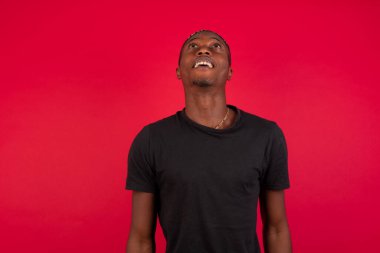 İnsanlar ve ani tepki kavramı. Şaşırmış Afrikalı Amerikalı erkek öğrenci, omuz silkiyor, yana bakıyor, arkadaşlarıyla yeni planları için mutlu ve heyecanlı. Duvarda izole edilmiş..