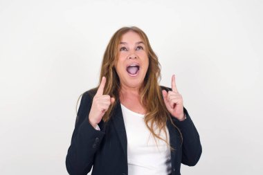 Olumlu ifadeli, kaygısız orta yaşlı bir kadın, her iki işaret parmağıyla işaret ediyor, günlük kıyafetler giymiş, geniş ilgi çekici bir gülümsemesi var, gri arka planda soyutlanmış. Şuraya bakın, lütfen..