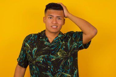 Endişeli ve endişeli İspanyol adam hiçbir şey hatırlamıyor. Kafası karışmış İspanyol bir adamın portresi, günlük giysiler giymiş, saçına el ele tutuşmuş, kaşlarını çatmış, paniklemiş, sarı duvar yüzünden hafızasını kaybetmiş.