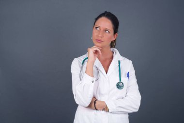 Yüz ifadeleri ve duygular. Düşünceli, genç, güzel bir doktor. Gri arka planda izole edilmiş, el ele tutuşmuş, şüpheli bakışları olan ve arkadaşının doğum günü partisinde ne giyeceğine karar veremeyen bir kadın..